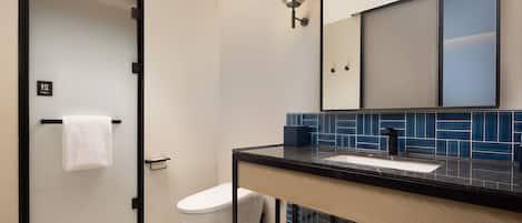 A modern bathroom with a glass shower door, a white toilet, a sink with a black countertop, and a mirror above the sink.