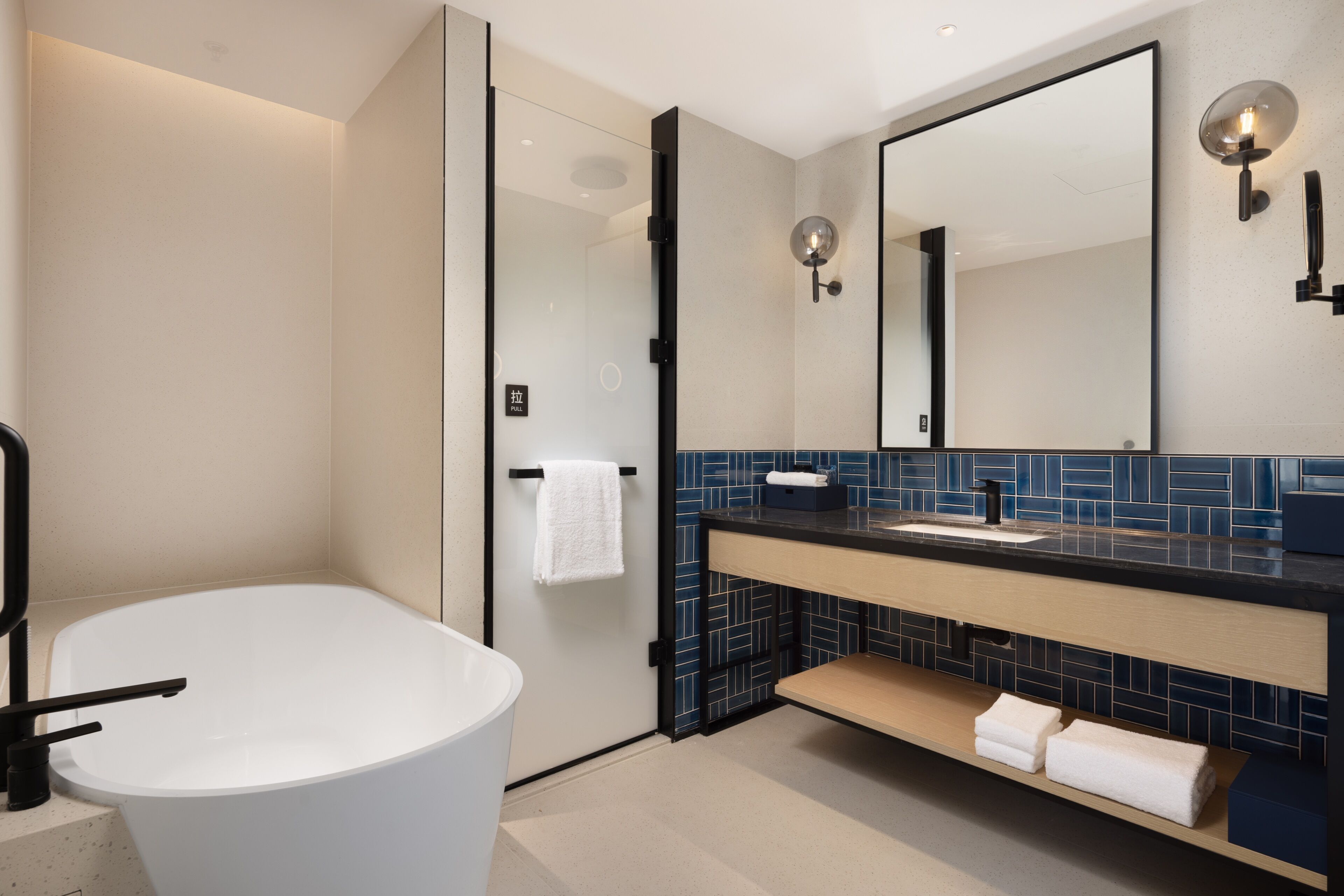 A modern bathroom with a freestanding bathtub, a large mirror, and a dark tiled backsplash.