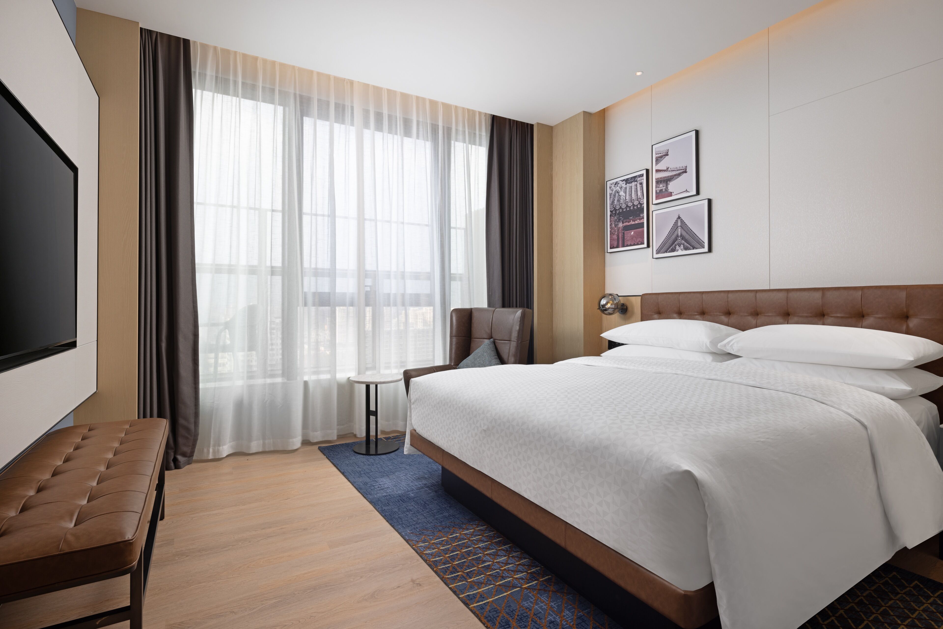 Ein Hotelzimmer mit einem großen Bett, einem Fernseher, einem Sessel und einem kleinen Tisch.