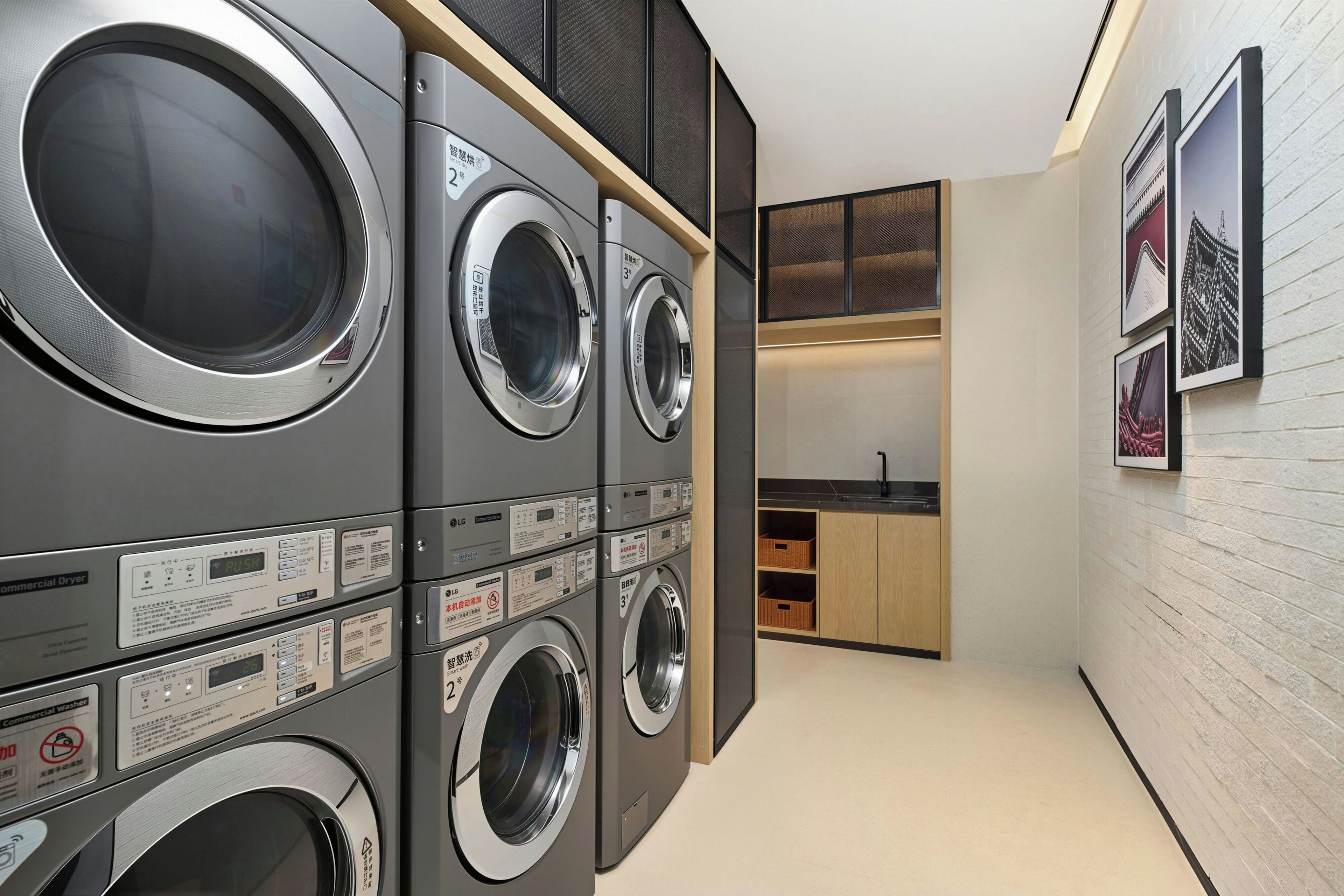 A laundry room with multiple stacked washing machines and dryers, wooden cabinets, and a small kitchenette area.
