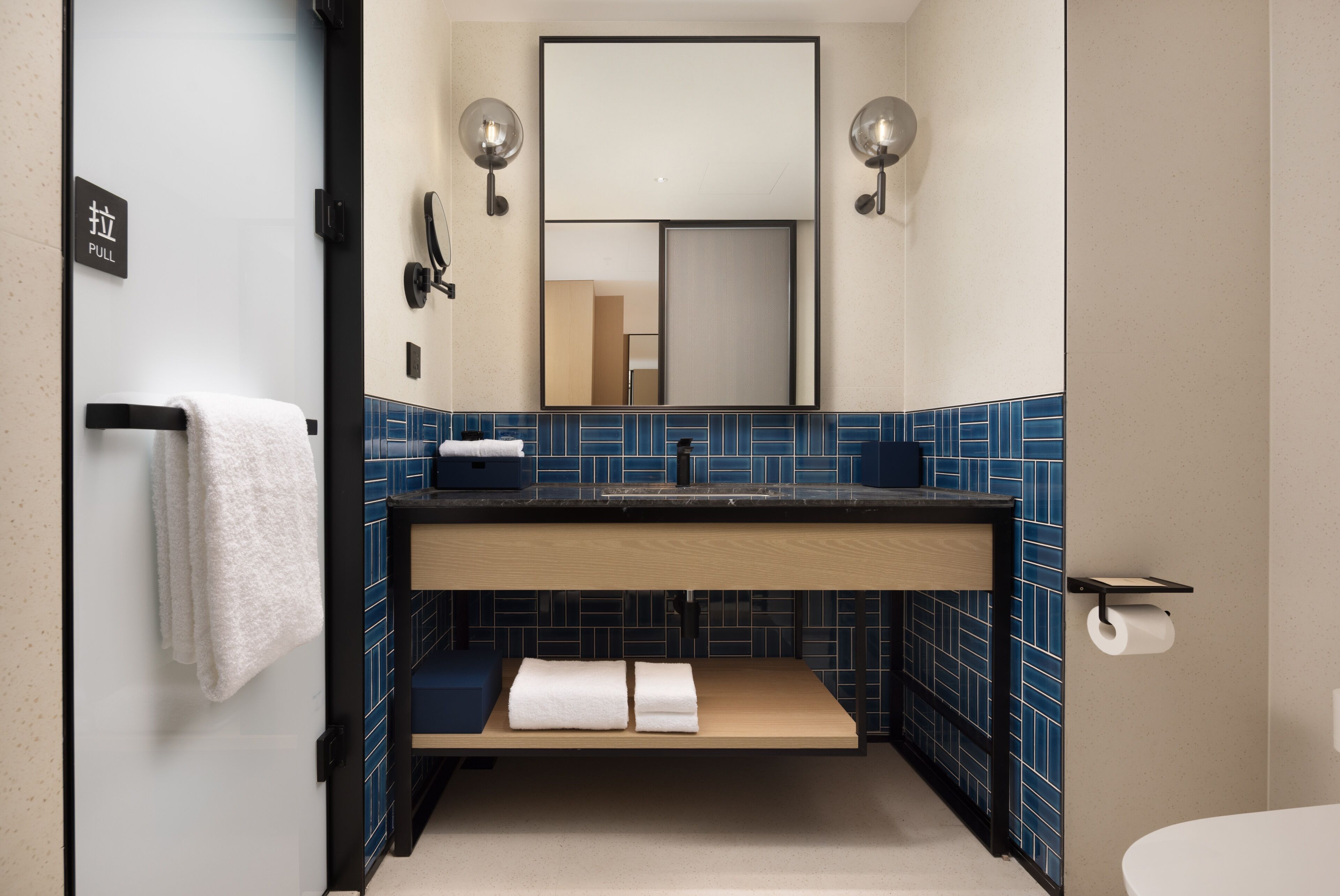 Un baño con lavamanos, espejo, toallero y pared de azulejos azules.