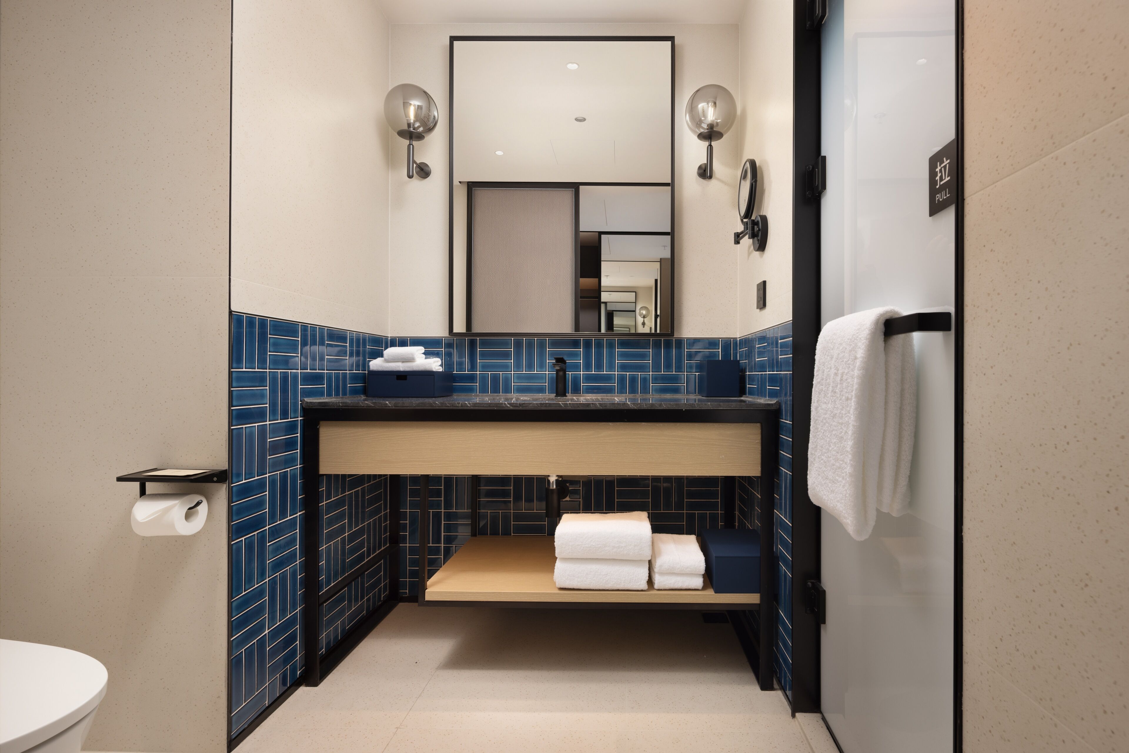 Ein Badezimmer mit Toilette, Waschbecken, Spiegel, Handtuchhalter und blauen Fliesen.