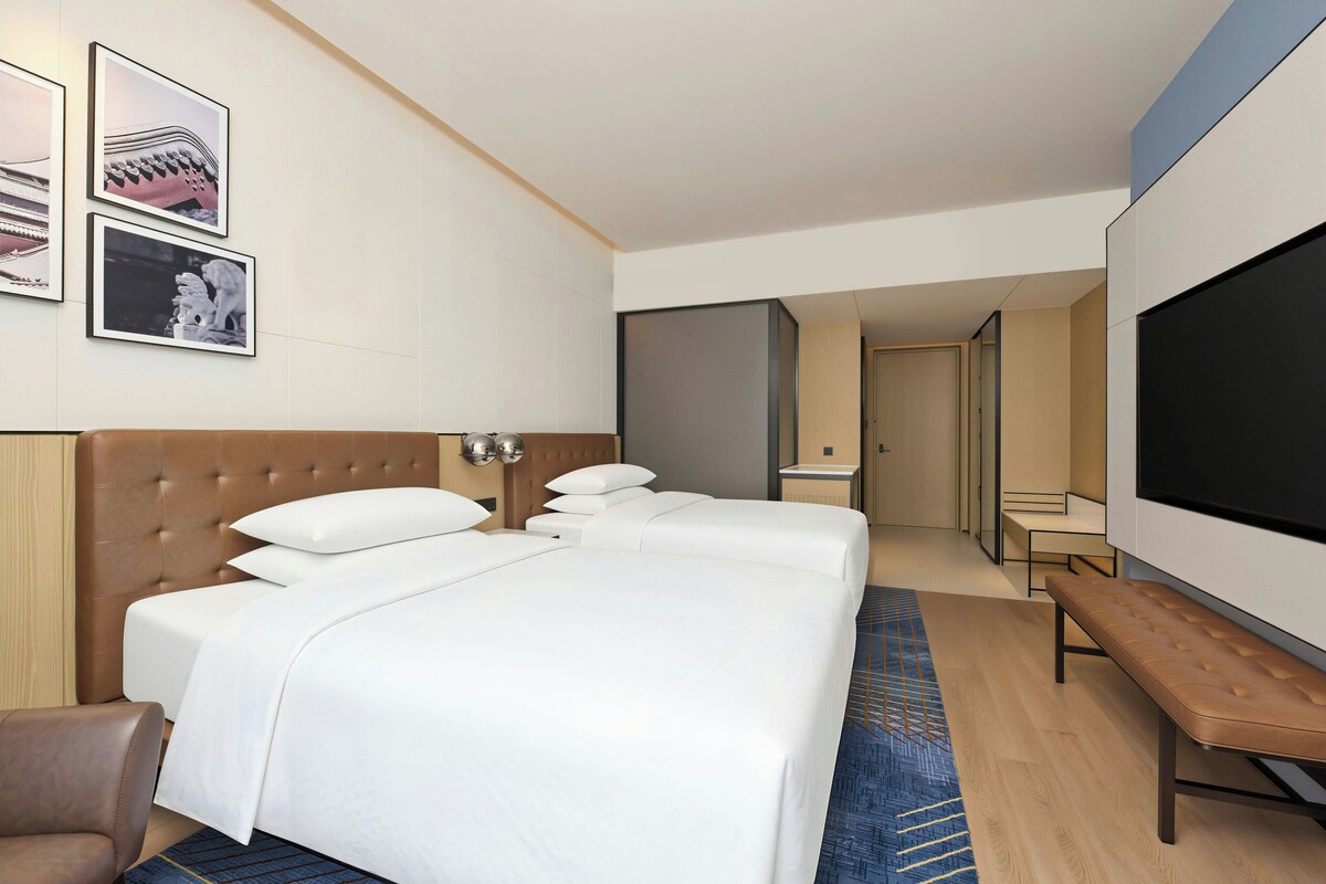 A hotel room with a large bed, a seating area, a television, and a bathroom visible through an open door.