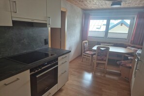 A compact kitchen with a stove, oven, and cabinets, a dining area with a table and chairs, and a window with a view of buildings. - Apartment with Whirlpool Bathtub in St. Anton (St. Anton am Arlberg)