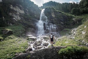 Une personne se tient sur un promontoire rocheux, surplombant une cascade dans une région montagneuse.