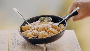 Kulho täynnä pastaa ja vieressä lusikka, kaikki puupöydällä.
