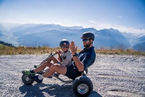 Dos personas en un vehículo pequeño con ruedas sobre un terreno pedregoso, con un paisaje montañoso al fondo.