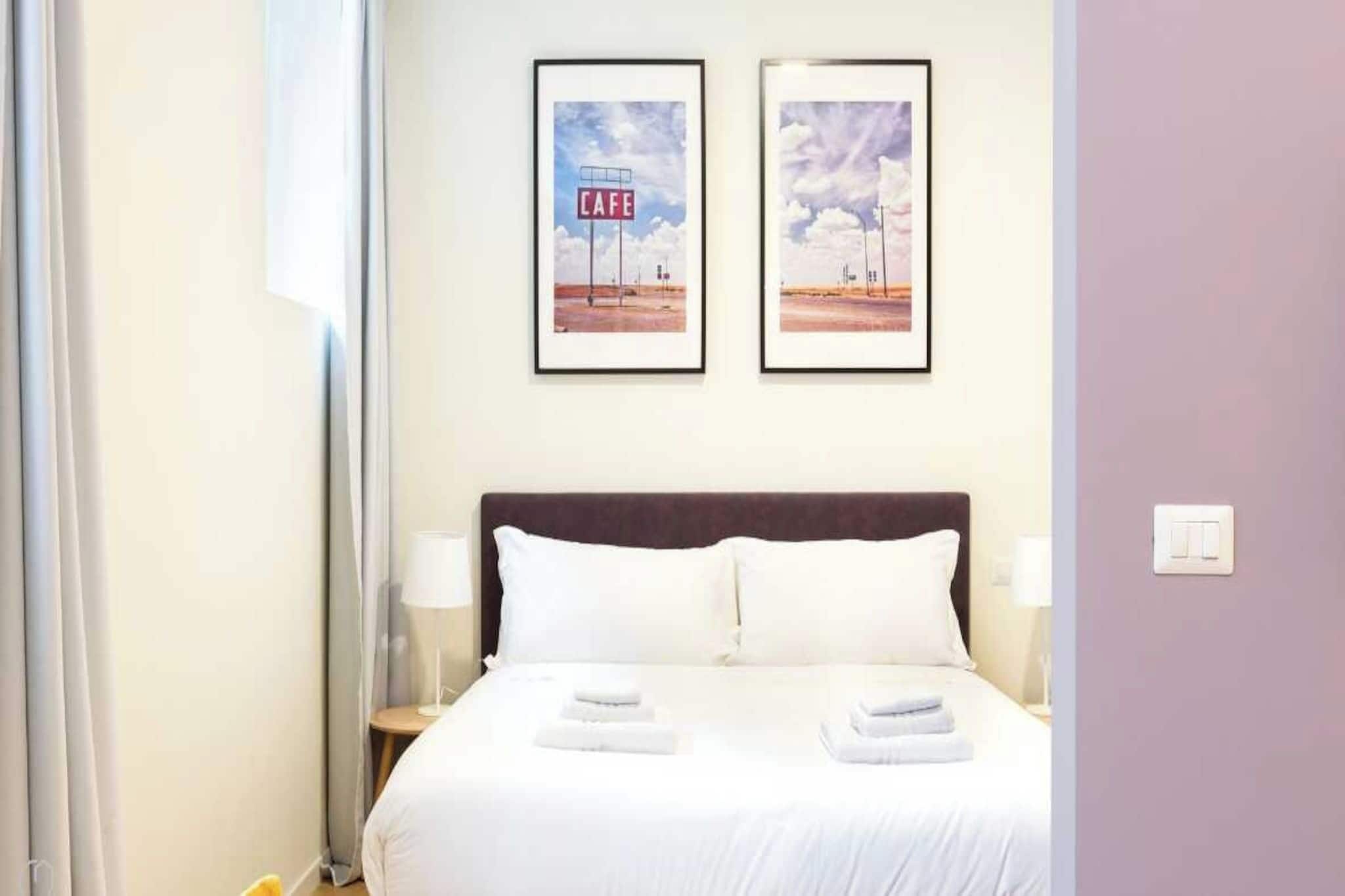 Ein Hotelzimmer mit einem Bett, zwei gerahmten Bildern an der Wand, einem Nachttisch und einer Lampe.
