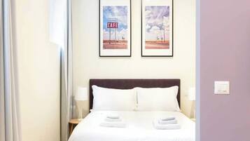 Ein Hotelzimmer mit einem Bett, zwei gerahmten Bildern an der Wand, einem Nachttisch und einer Lampe.
