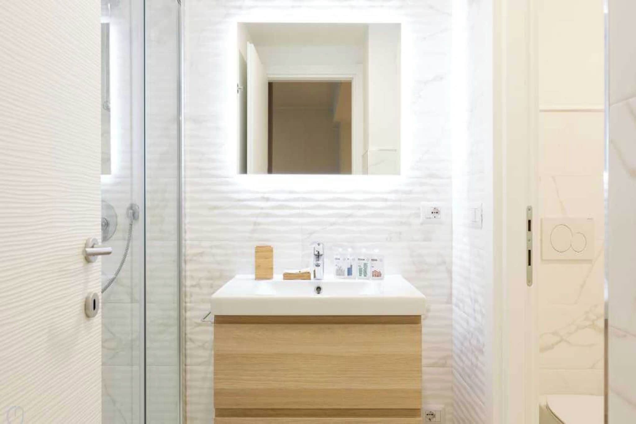 Un baño con cabina de ducha de vidrio, un lavabo blanco sobre mueble de madera y un espejo sobre el lavabo.