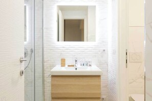 Un baño con cabina de ducha de vidrio, un lavabo blanco sobre mueble de madera y un espejo sobre el lavabo.