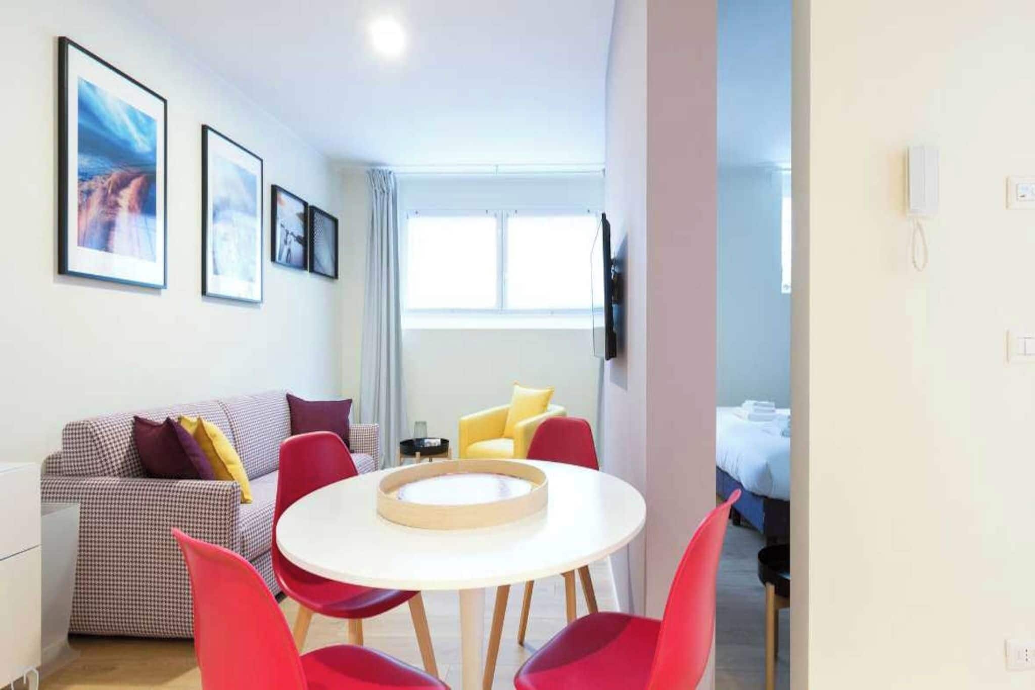 Ein modernes Hotelzimmer mit einer karierten Couch, roten Stühlen, einem runden Tisch und gerahmten Bildern an der Wand.
