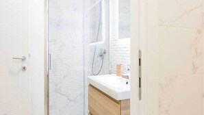Ein Badezimmer mit Duschkabine aus Glas, einem weißen Waschbecken und Holzschränken.