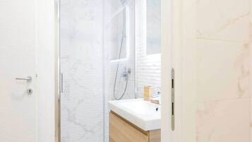A bathroom with a glass shower enclosure, a white sink, and wooden cabinetry.