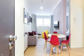 A modern living room with a sofa, a round table, and red chairs. There is a television mounted on the wall and a window with curtains. - Charming Studio 4P - Milano Centrale (Milano)