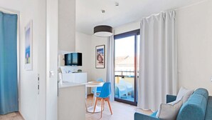 Ein modernes Wohnzimmer mit einer Couch, einer Essecke mit Tisch und Stühlen, einem Fernseher und einem Balkon mit Vorhängen.