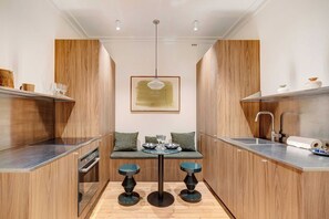 Una cocina moderna con armarios de madera, una isla central con taburetes, una lámpara colgante y una obra de arte enmarcada en la pared.