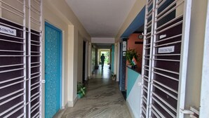 A corridor with metal gates, a blue door, and a person walking away. - A India Guest House (Mohanpur)