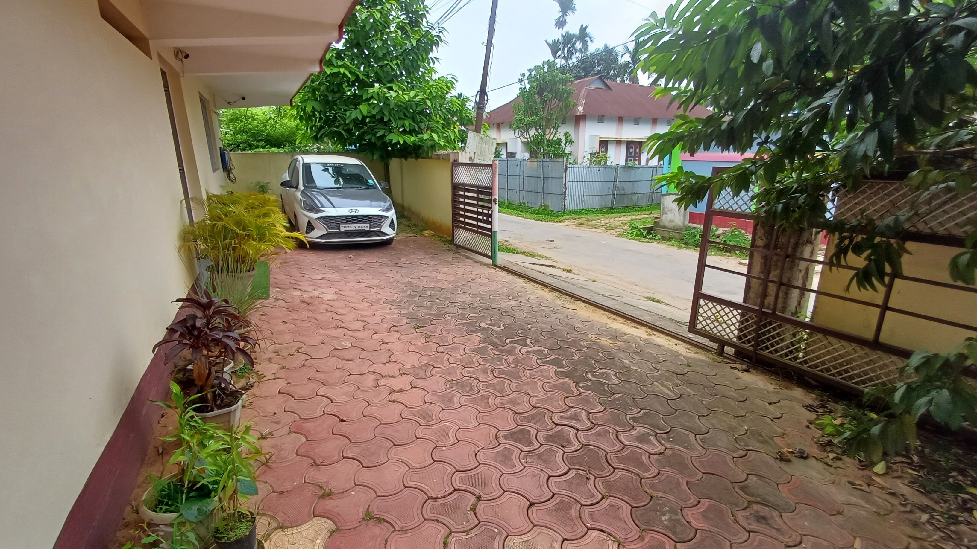 A paved driveway leading to a gated entrance, a parked car, and a house with a red roof.