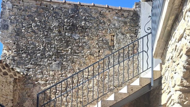 Una escalera de piedra con barandillas de metal que baja a un nivel inferior.