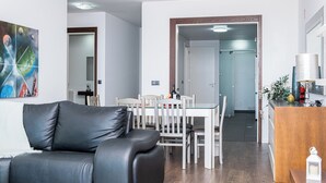 En moderne stue med en sort lædersofa, et spisebord med hvide stole og et træskab.