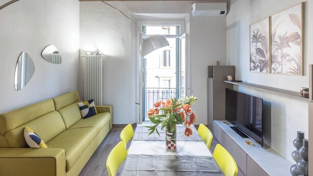 A living room with a sofa, dining table, chairs, a TV, and a vase of flowers. - Indipendenza (Bologna)