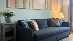 Ein Wohnzimmer mit einem dunkelblauen Sofa, einem kleinen Beistelltisch mit Blumenvase und einem großen abstrakten Gemälde an der Wand.