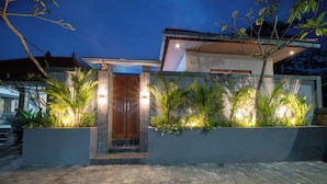 Uma casa moderna com entrada pavimentada, porta de madeira e plantas iluminadas.
