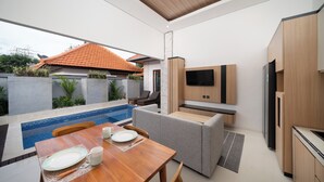 Uma cozinha moderna com eletrodomésticos embutidos, um espaço de refeições com vista para a piscina e uma TV fixada na parede.
