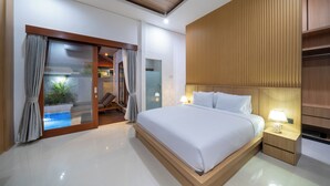 Quarto de hotel moderno com uma cama grande, mesa de cabeceira com abajur, porta de vidro deslizante para uma varanda e cabeceira de madeira.