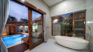 Um banheiro moderno com uma banheira independente, chuveiro com box de vidro e uma piscina visível através das portas de vidro.