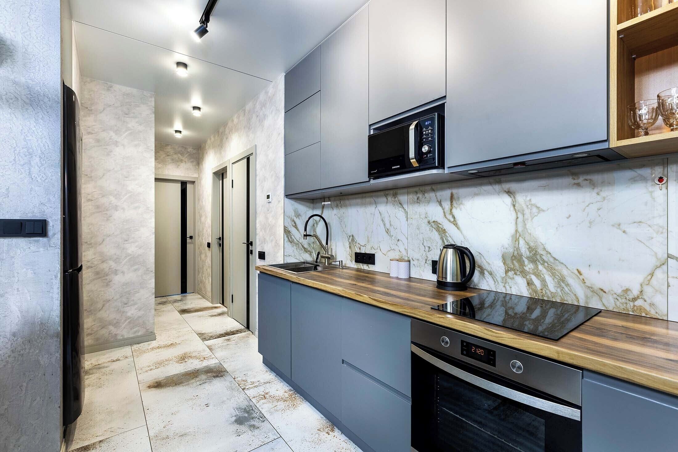 A modern kitchen with a marble backsplash, stainless steel appliances, and a wooden countertop.