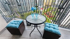 Uma varanda com mesa de vidro e duas cadeiras estofadas, um vaso com flores e vista para o horizonte urbano.