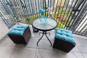 Un balcón con una mesa de vidrio y dos sillas acolchadas, un jarrón con flores y vistas a la ciudad.