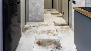 Um corredor central ladeado por portas, eletrodoméstico de aço inoxidável à esquerda e parede de mármore com luminária embutida.