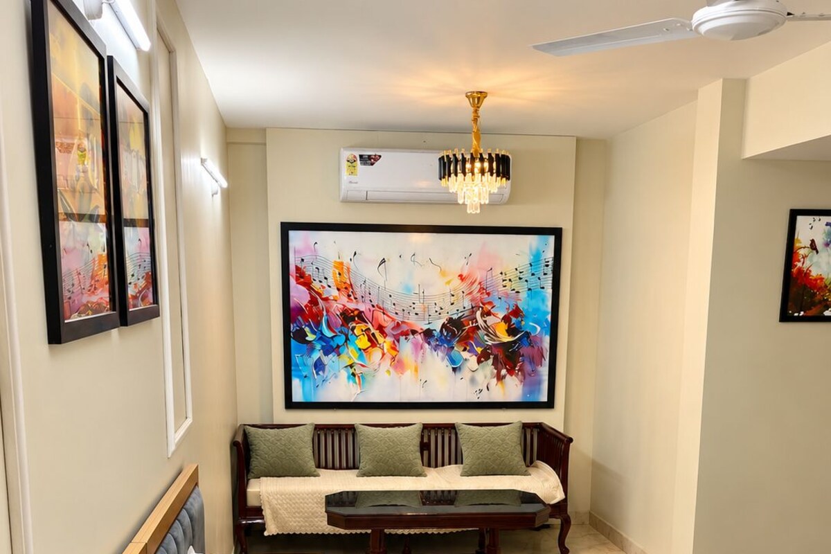 A hotel room with a bed, a seating area, a large abstract painting, and an air conditioning unit.