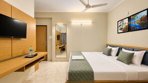 A hotel room with a bed, a TV, a mirror, and artwork on the wall.
