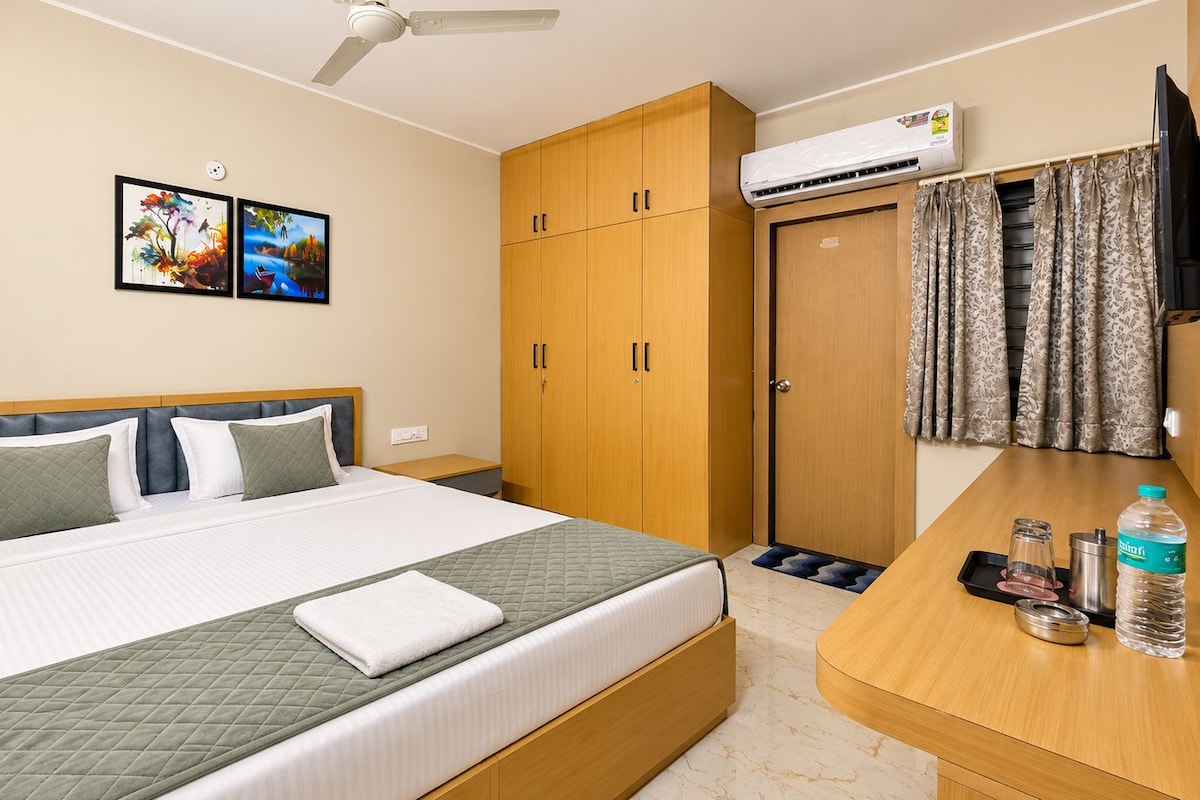 A hotel room with a bed, a desk, an air conditioning unit, and a wardrobe.