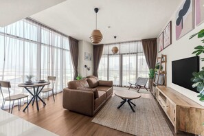 A modern living room with a sofa, coffee table, and chairs. There is a TV on the wall and a large window with curtains. - Modern 1BR in Prime Business Bay | Sleeps 2 - StayShort (Business Bay)
