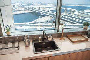 A kitchen with a modern sink, a window with a view of a cityscape and waterway, and a potted plant on the counter. - Modern 1BR in Prime Business Bay | Sleeps 2 - StayShort (Business Bay)