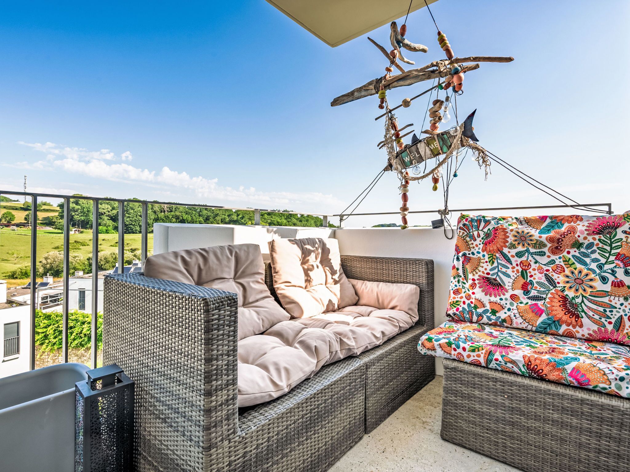 A balcony with wicker furniture, a hanging decoration, and a view of greenery.