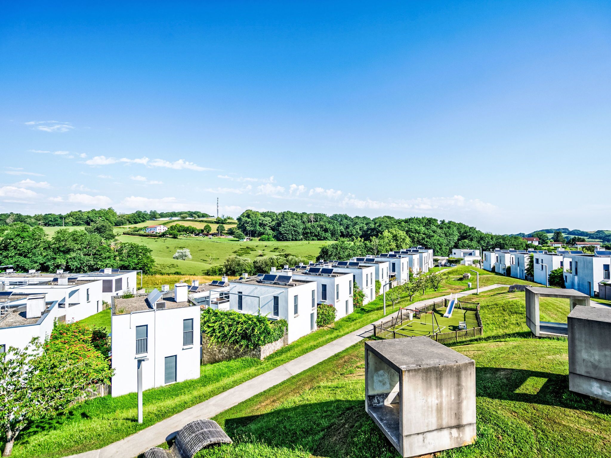 Une rangée de maisons mobiles modernes, blanches, dotées de panneaux solaires sur les toits, s’étend au milieu d’un paysage verdoyant sous un ciel dégagé.