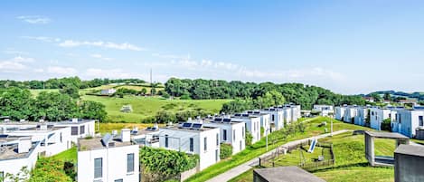 Une rangée de maisons mobiles modernes, blanches, dotées de panneaux solaires sur les toits, s’étend au milieu d’un paysage verdoyant sous un ciel dégagé.