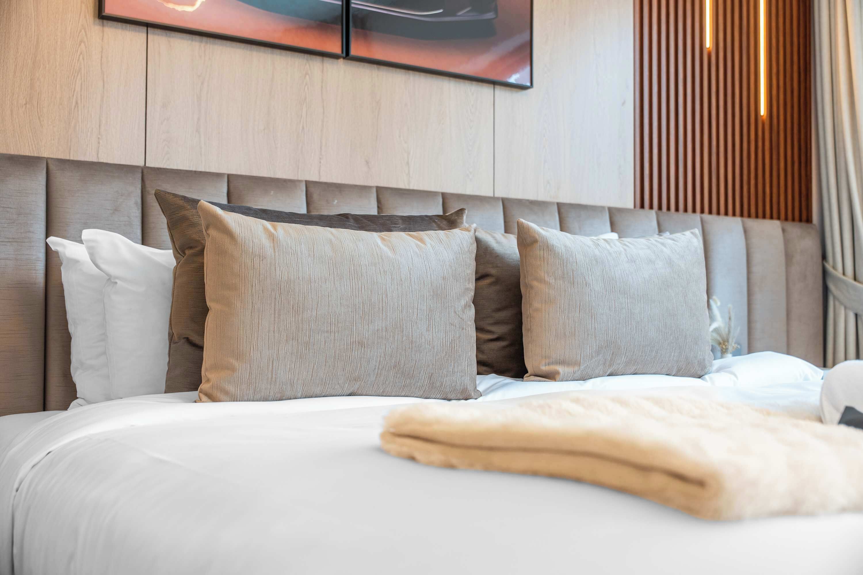 A neatly made bed with a white comforter and a beige throw blanket.