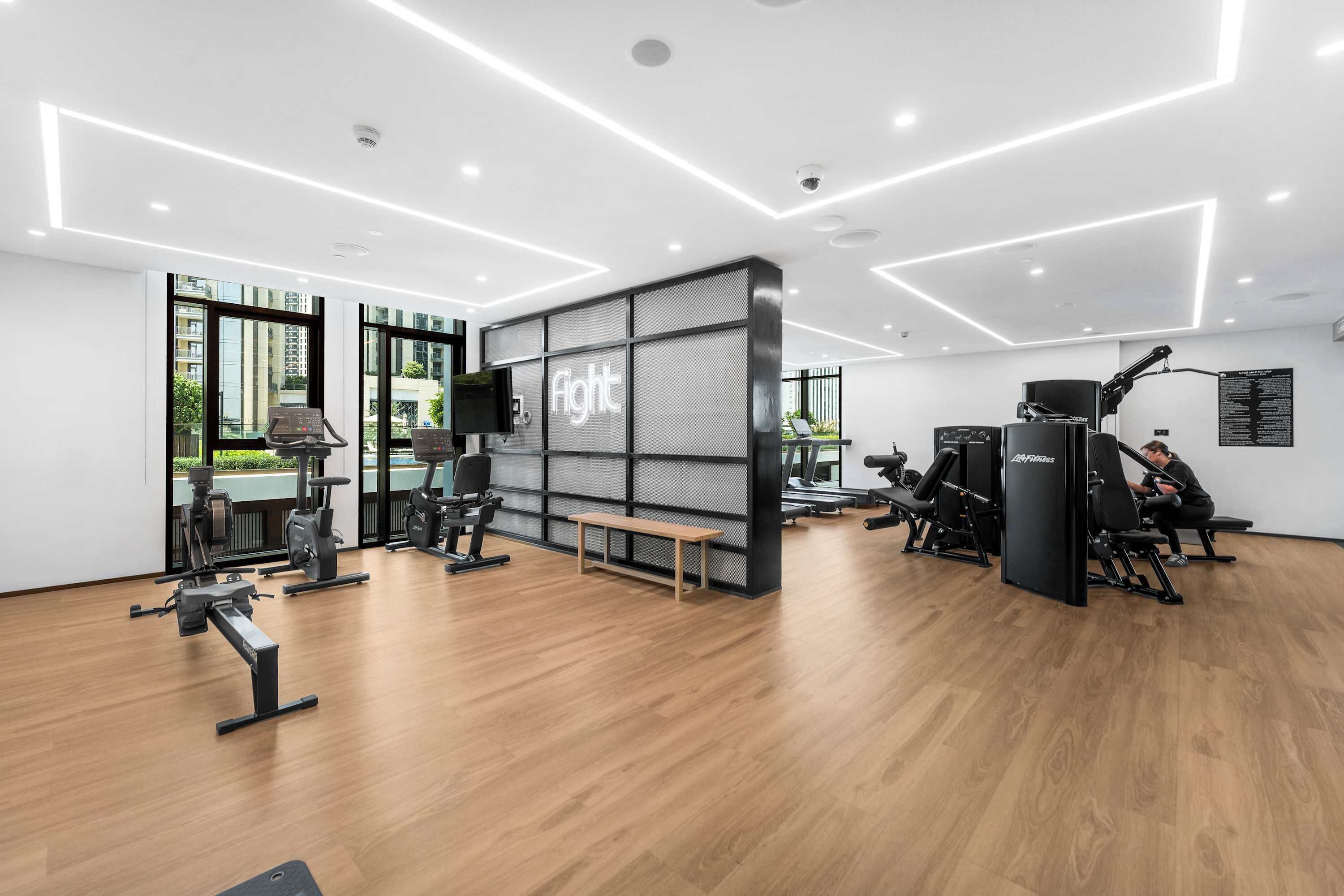 A modern gym with exercise equipment, a bench, and a wall-mounted TV.