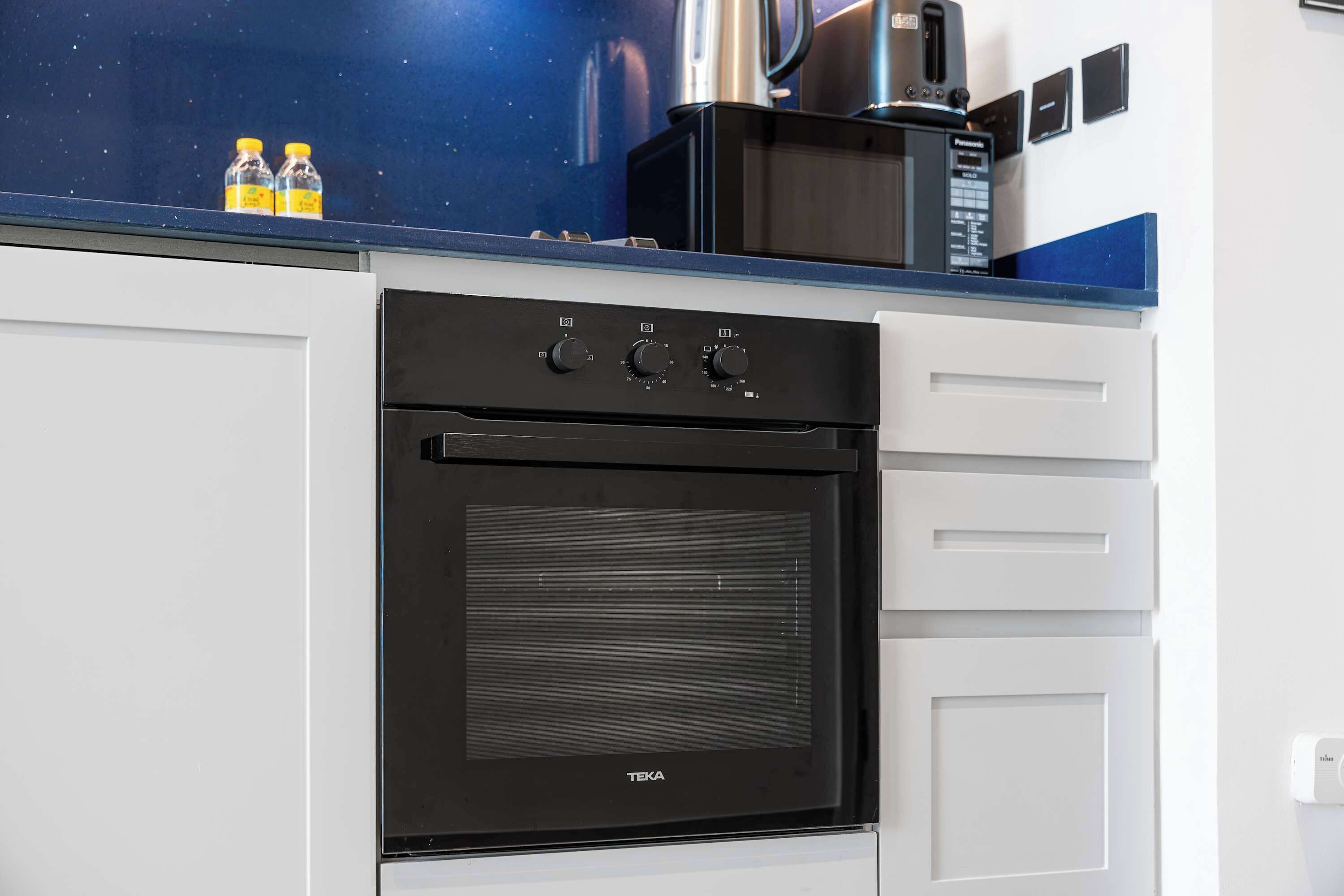 Una cucina con forno nero, mobili bianchi e un piano di lavoro blu.
