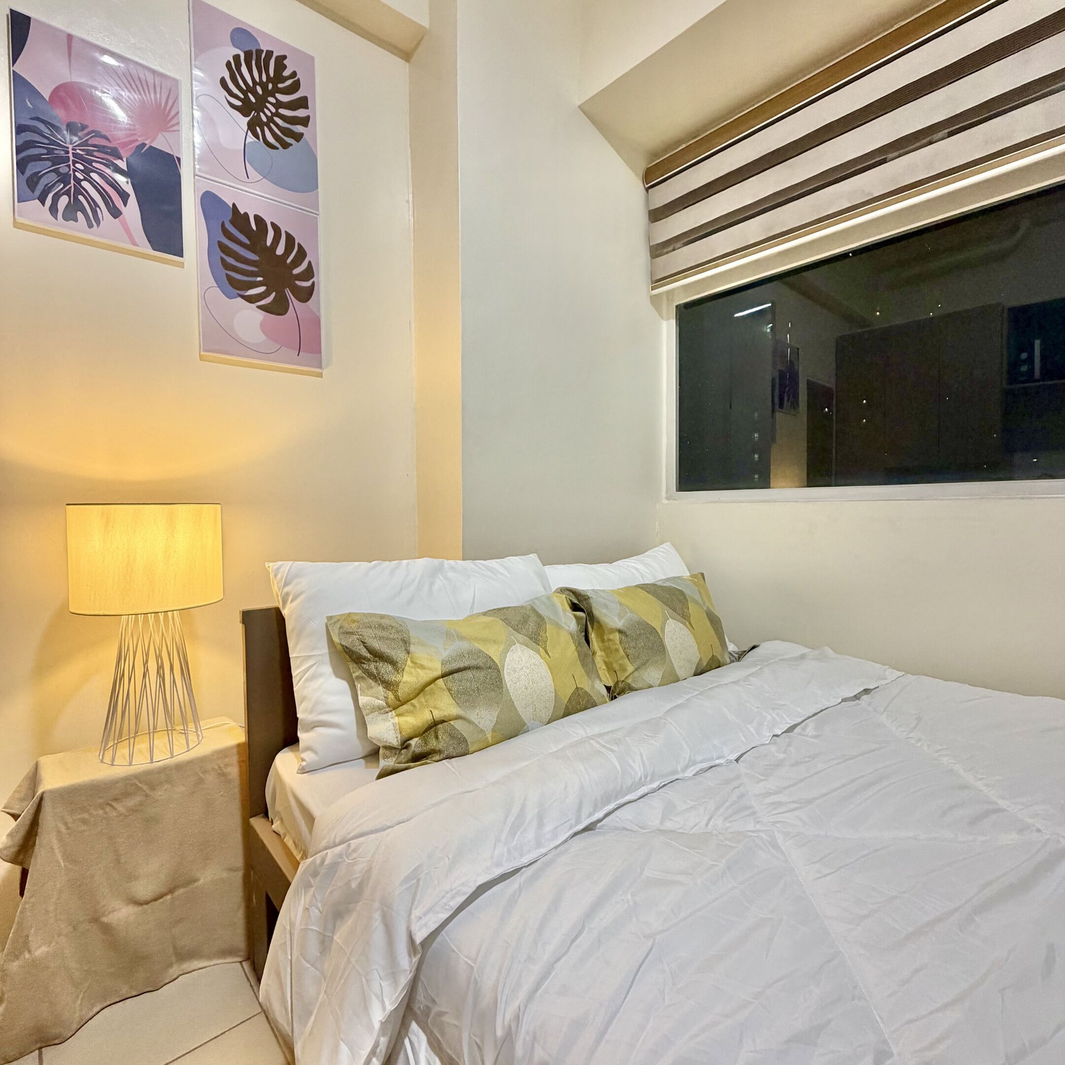 Une chambre à coucher comprenant un lit, une table de chevet, une lampe et des œuvres d’art murales.