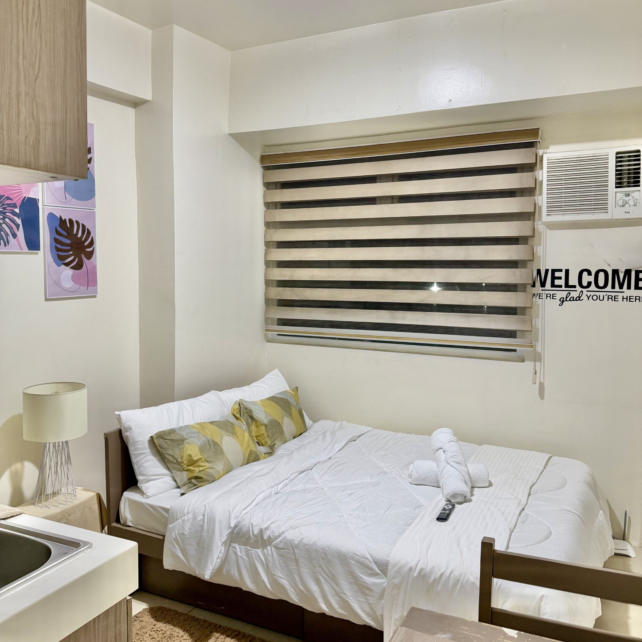 A hotel room with a bed, a desk, a lamp, and a window with blinds.