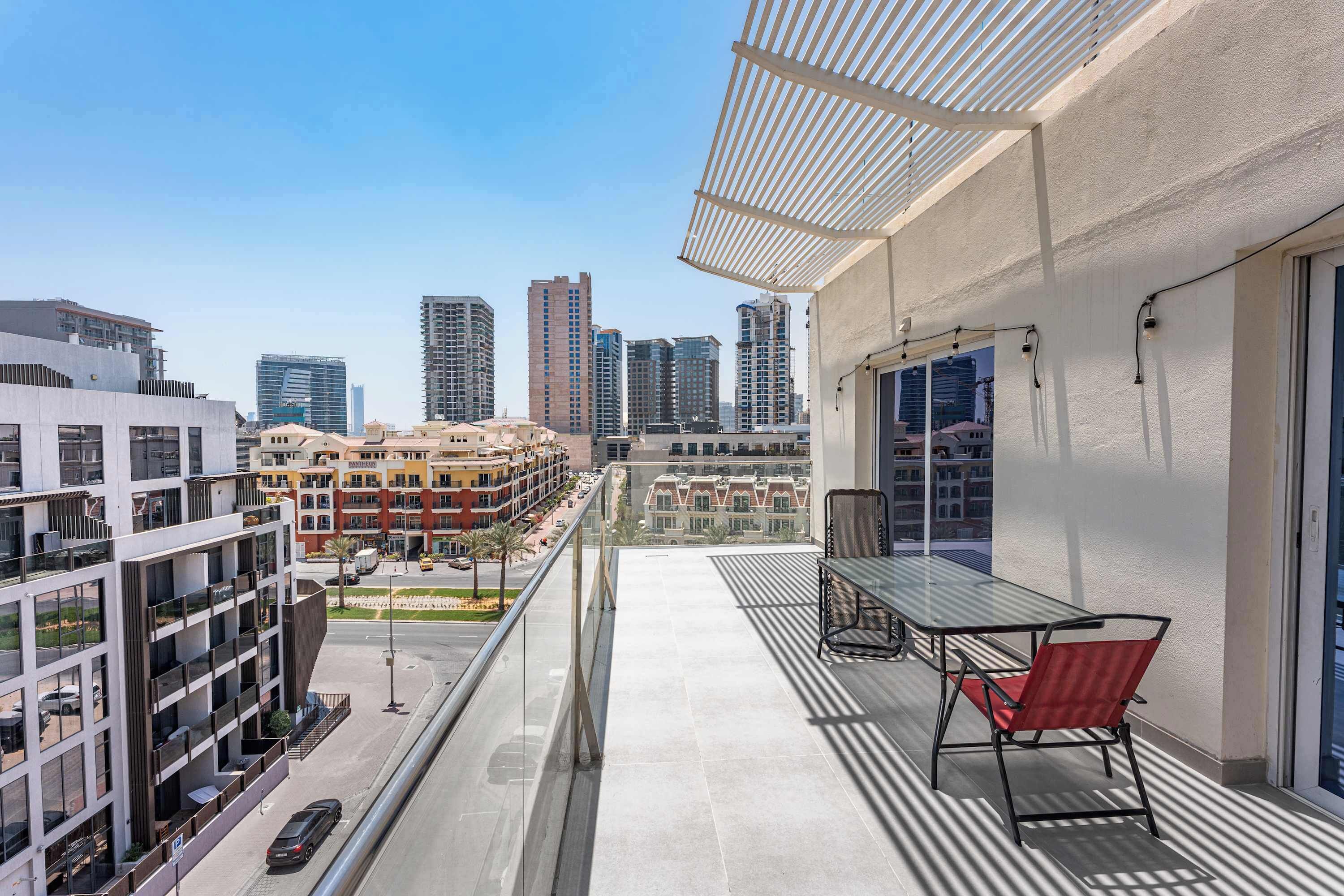 Un balcone con ringhiera in vetro, un tavolo e una sedia, con vista su un panorama urbano caratterizzato da grattacieli.