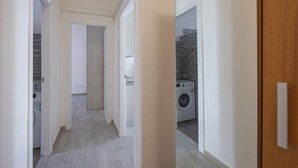 Een hal met een wasmachine, een deur naar een wasserij en een houten deur aan de rechterkant.